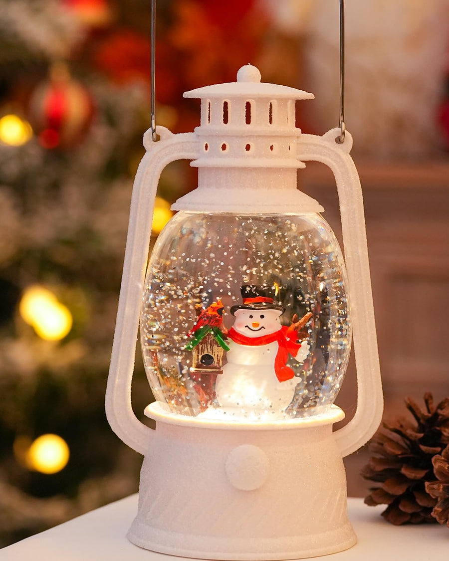 White lantern snow globe with a snowman in a red scarf, lit up beside a pinecone